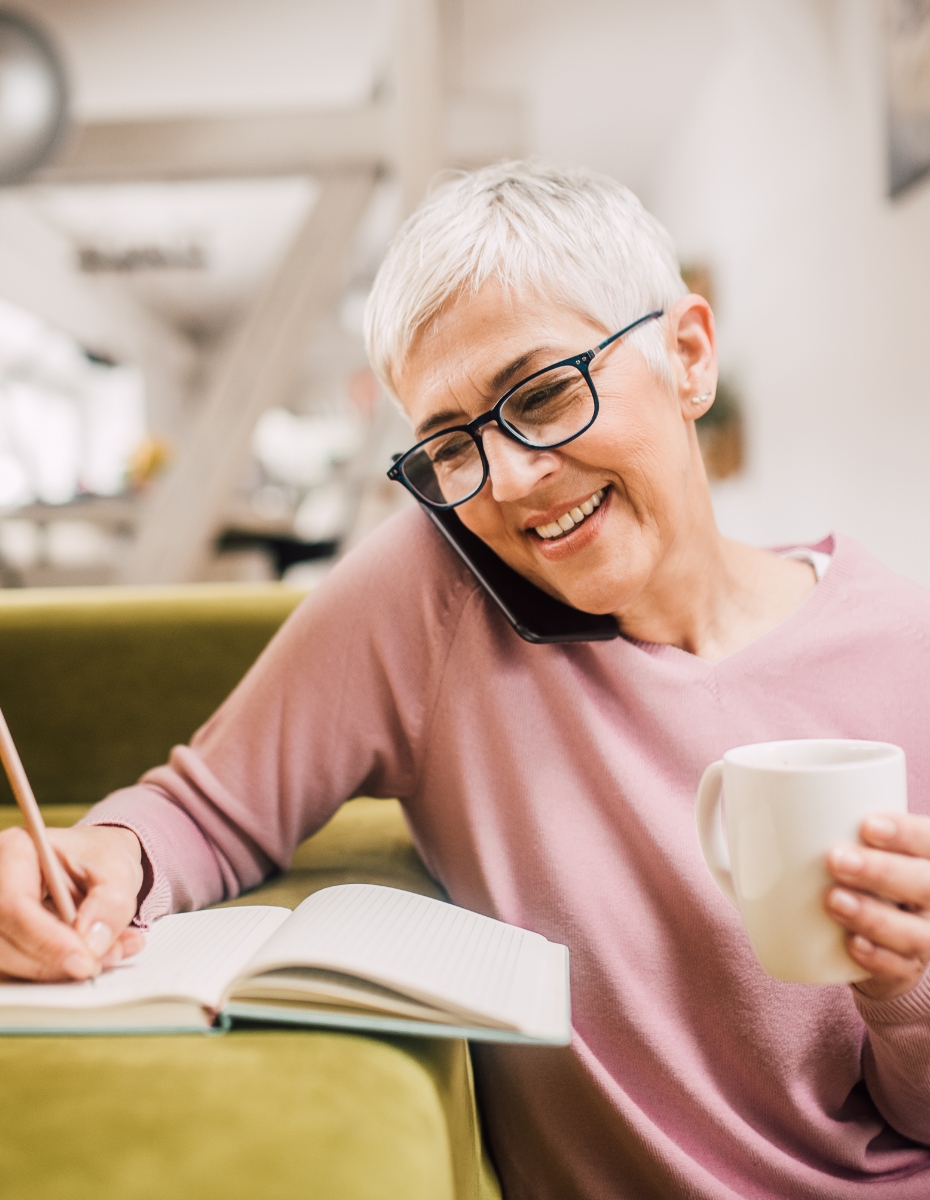 Frau mit Brille telefoniert und macht beim Telefonat Notizen.